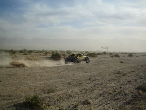 Yellow off-road buggy trailing dust on a hazy desert course at a distance