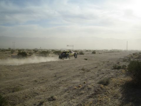 Distant off-road buggy raising dust on a hazy desert plain