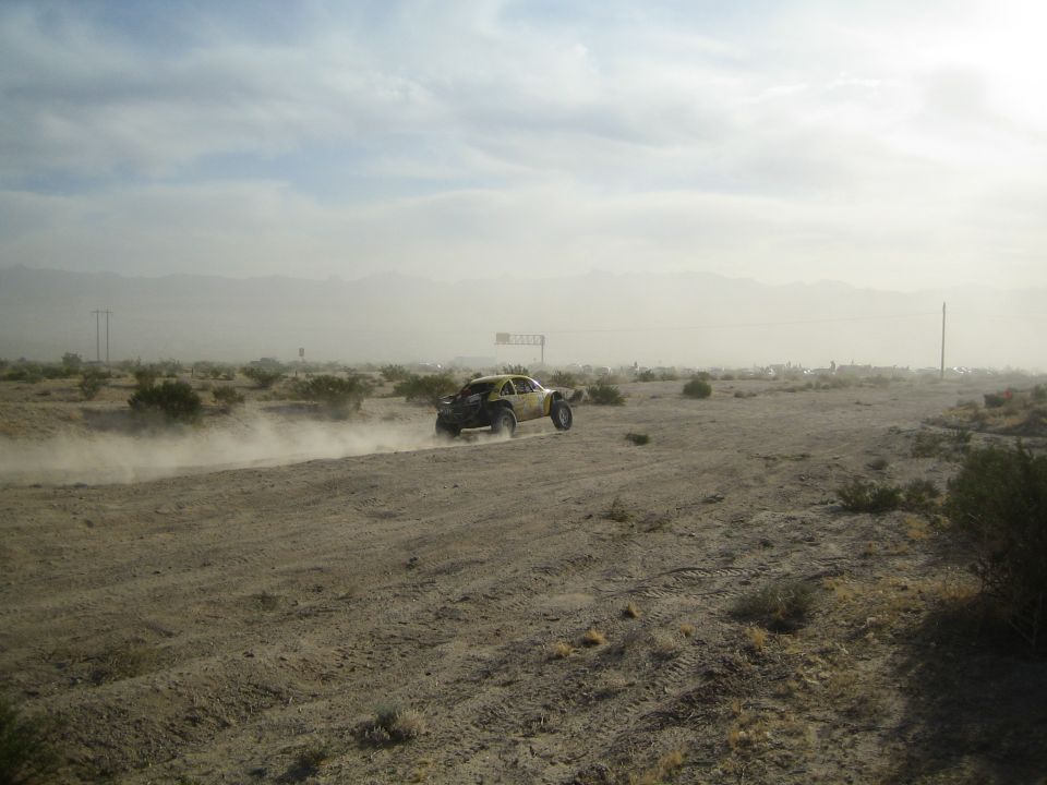 Distant off-road buggy raising dust on a hazy desert plain