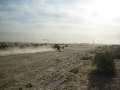 Distant off-road buggy on a dusty desert track near a billboard sign