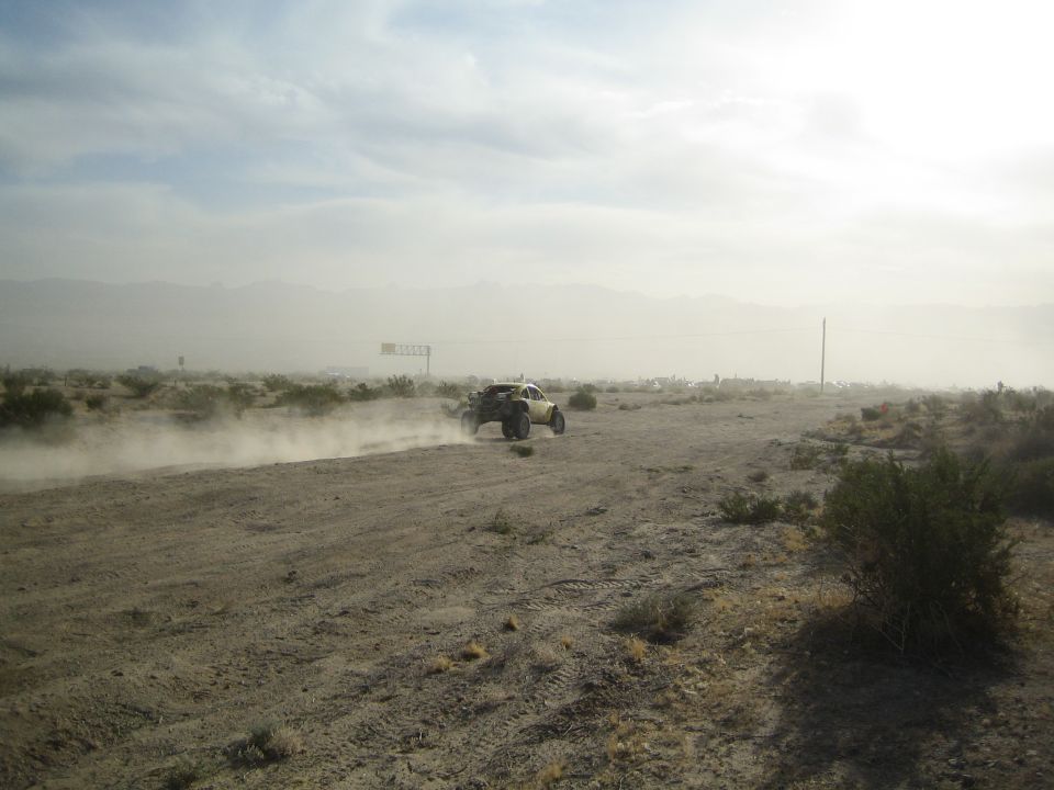Distant off-road buggy on a dusty desert track near a billboard sign