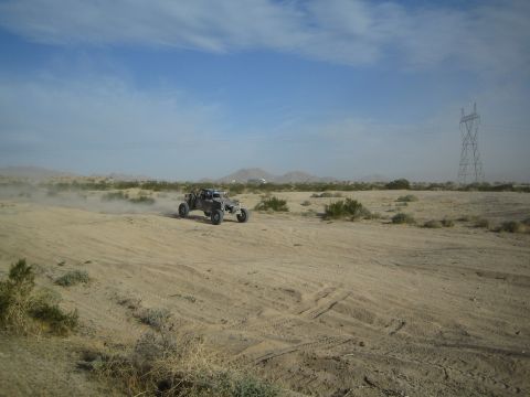 Dark off-road buggy crossing sandy desert near a transmission tower