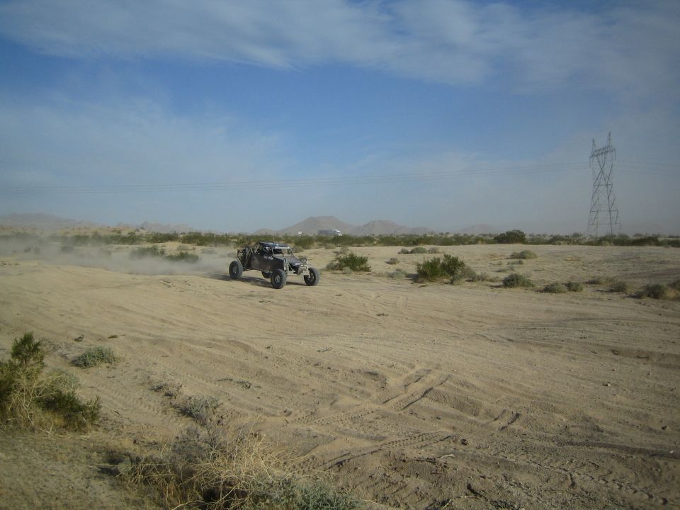 Dark off-road buggy crossing sandy desert near a transmission tower