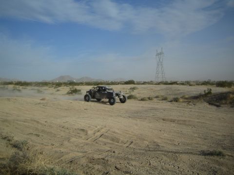 Dark off-road buggy on a sandy desert rise below a transmission tower