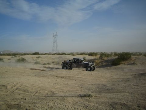 Black off-road race buggy kicking up dust on a desert dirt track near power lines