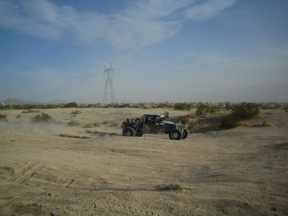 Black off-road race buggy kicking up dust on a desert dirt track near power lines