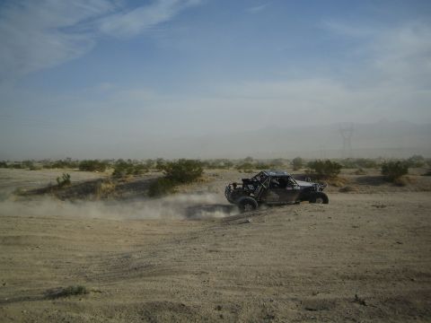 Dark off-road desert buggy racing across hazy sandy terrain trailing dust