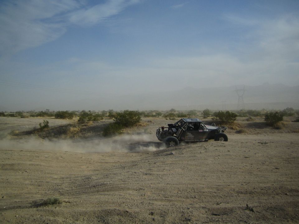 Dark off-road desert buggy racing across hazy sandy terrain trailing dust