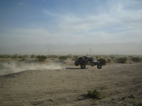 Off-road race buggy cresting a sandy berm in dusty desert under hazy sky