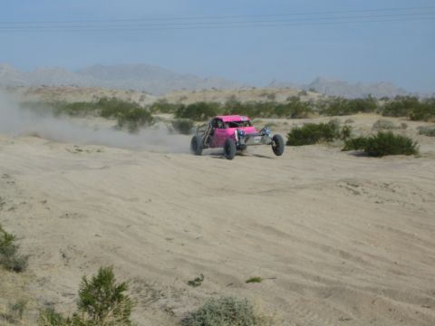 Pink and silver off-road buggy on a sandy desert rise trailing dust