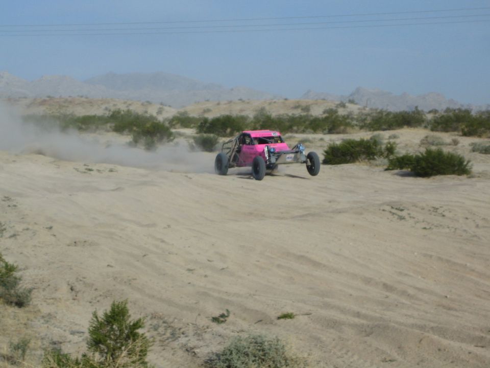 Pink and silver off-road buggy on a sandy desert rise trailing dust