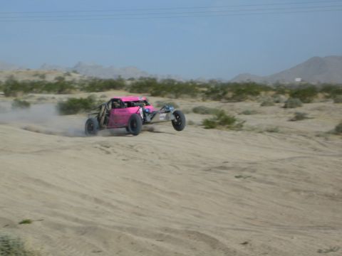 Pink off-road race buggy at speed across desert sand with motion blur