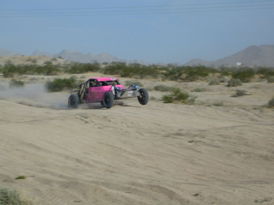 Pink off-road race buggy at speed across desert sand with motion blur