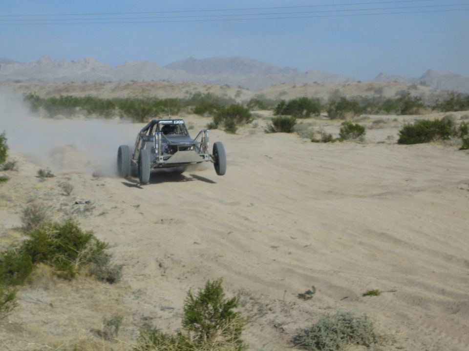 Silver tube-frame off-road buggy cresting a desert dune trailing dust