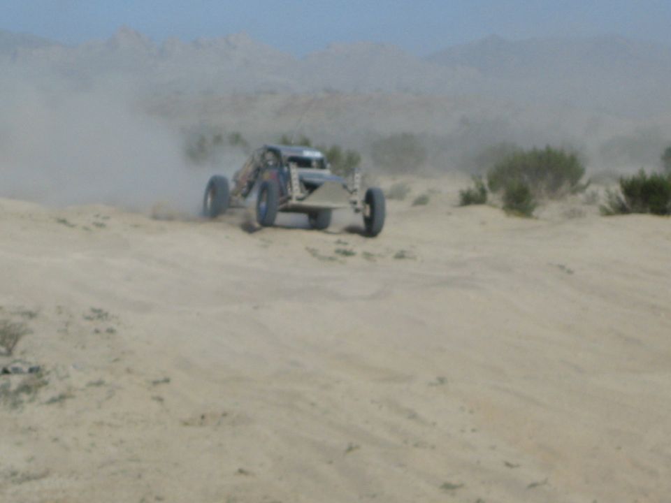Front view of silver off-road race buggy bouncing through dusty desert