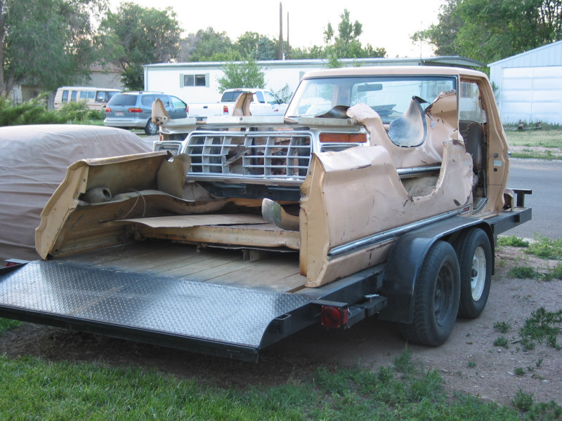Ford F-Series truck body, missing doors and hood, on a trailer. Grille is visible