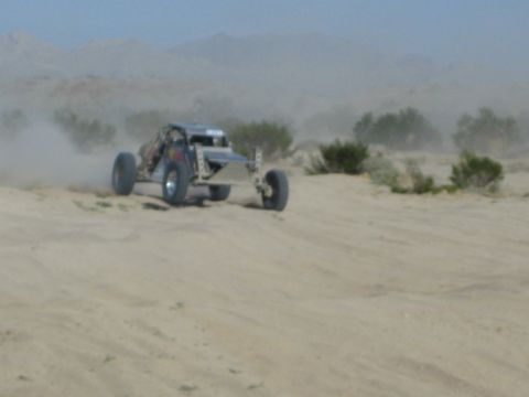 Silver off-road buggy with rear wheels lifting on a sandy desert rise