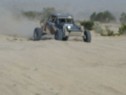 Front view of off-road race buggy with headlight on cresting a desert dune