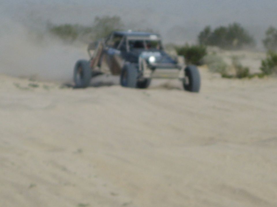 Front view of off-road race buggy with headlight on cresting a desert dune