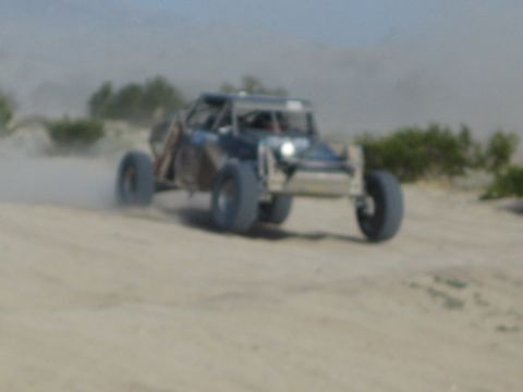 Off-road race buggy with headlight on charging through dusty desert