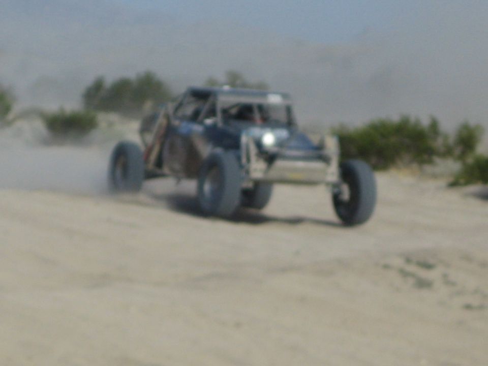 Off-road race buggy with headlight on charging through dusty desert