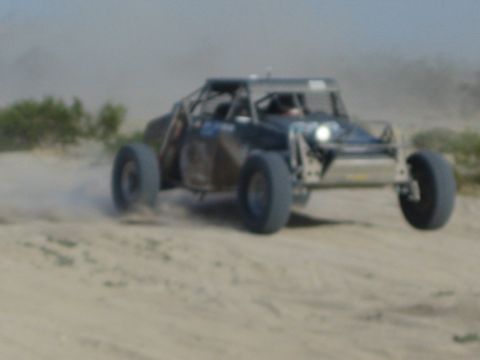 Dark off-road race buggy with headlight on driving across dusty desert