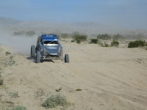 Blue off-road race buggy on a sandy desert track trailing dust