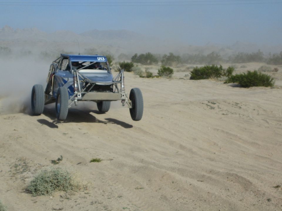 Blue off-road race buggy jumping over a sandy desert rise