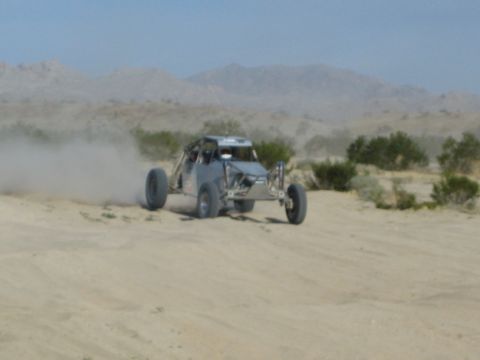 Gray off-road race buggy sliding across desert sand trailing dust