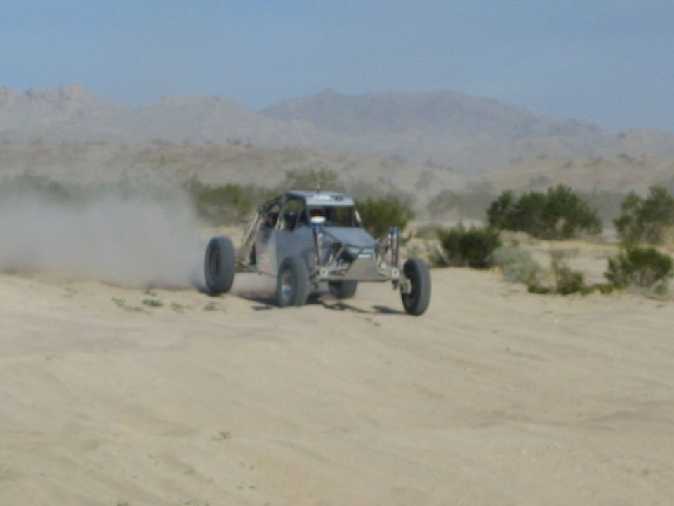 Gray off-road race buggy sliding across desert sand trailing dust