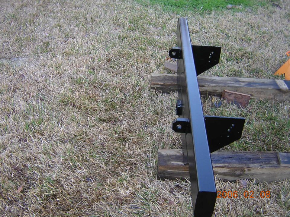 black metal bumper with mounting brackets, resting on wooden beams outdoors