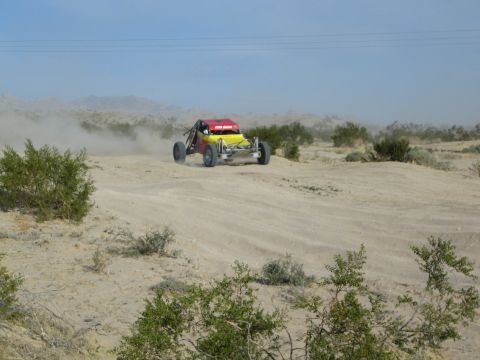 Red and yellow off-road buggy cresting a sandy desert berm in dust