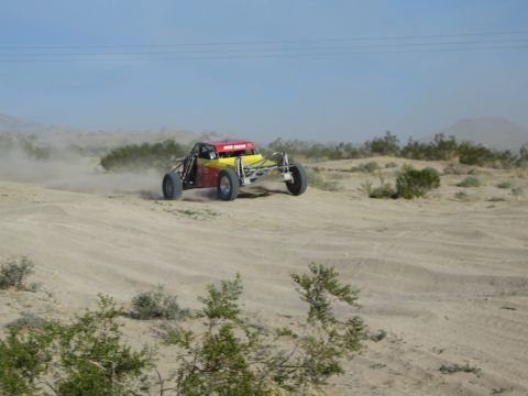 Red and yellow off-road buggy catching air over a desert rise