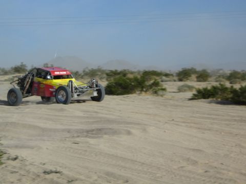Red and yellow off-road race buggy speeding across flat desert sand