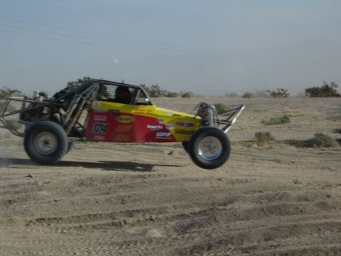Yellow and red off-road buggy number 124 with front wheel lifting in desert