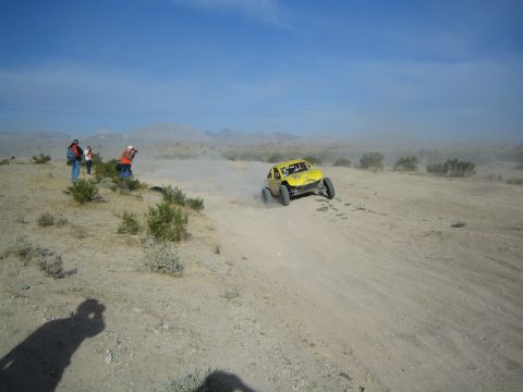 Yellow off-road race buggy passing spectators on a dusty desert track