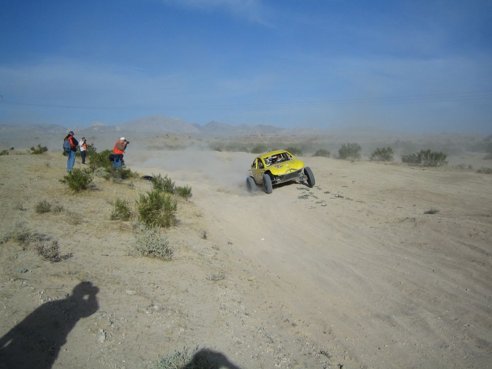 Yellow off-road race buggy passing spectators on a dusty desert track