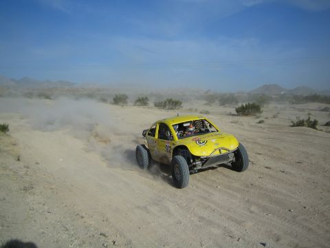 Yellow Baja-style race car number 502 racing through desert sand