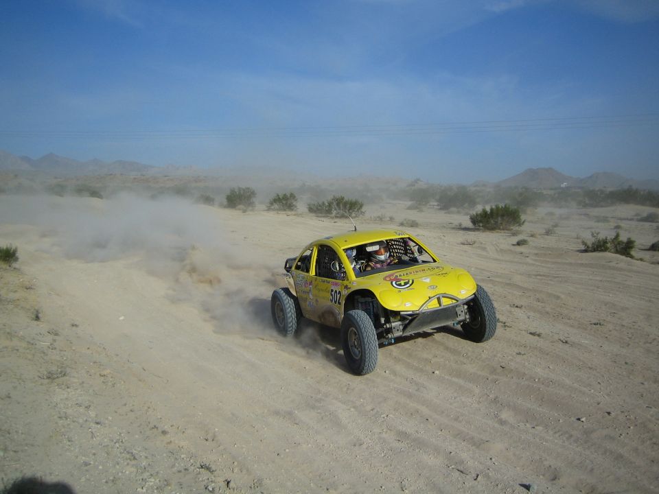 Yellow Baja-style race car number 502 racing through desert sand