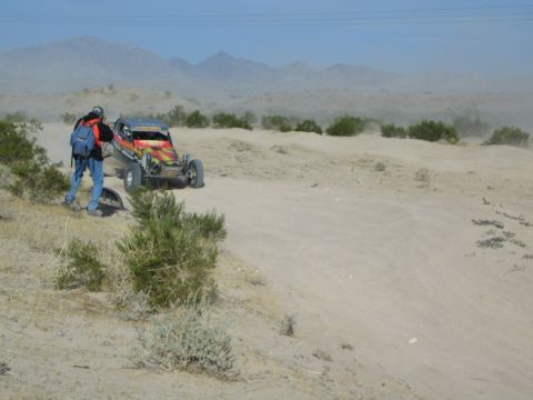Spectator in backpack photographs a red flame-painted race buggy in the desert