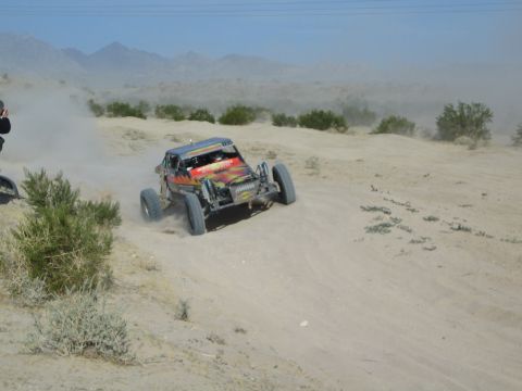 Red and yellow off-road race buggy cresting a sandy berm in the desert