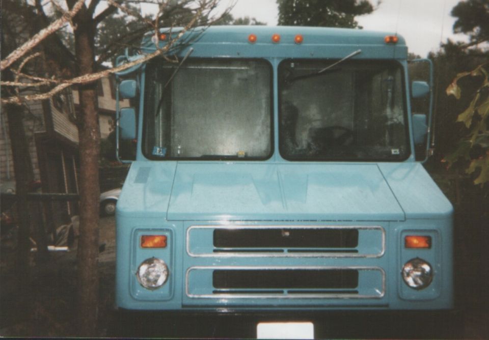 Front view of a light blue step van parked outdoors. It has a large grille and dual windshield wipers
