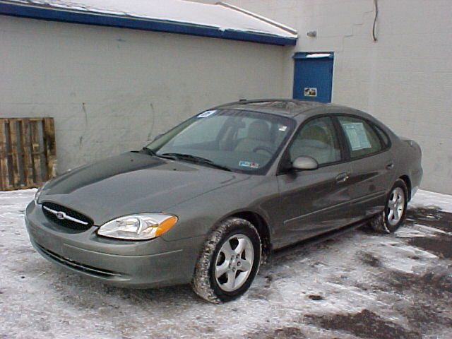 Gray-green Ford Taurus sedan, front three-quarter view, parked in snow by a white building