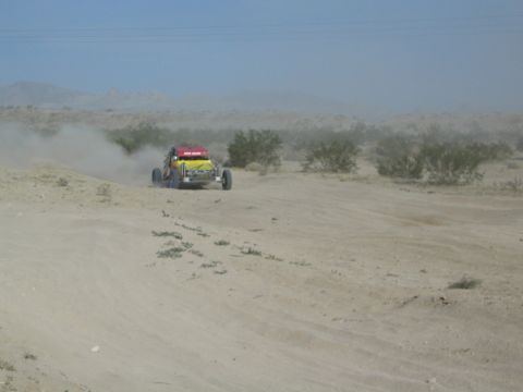 Distant yellow and red race buggy raising dust on an open desert course
