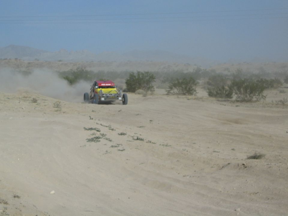 Distant yellow and red race buggy raising dust on an open desert course