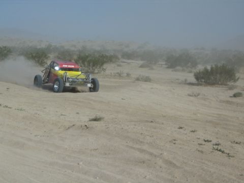 Yellow and red off-road buggy rounding a sandy berm in the desert