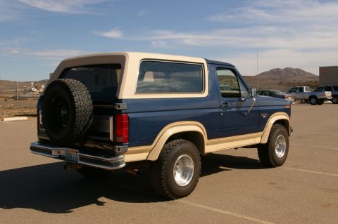 1986 Ford Bronco - This blue and tan Ford Bronco is viewed from the rear three-quarter angle, with a spare tire mounted on the back.