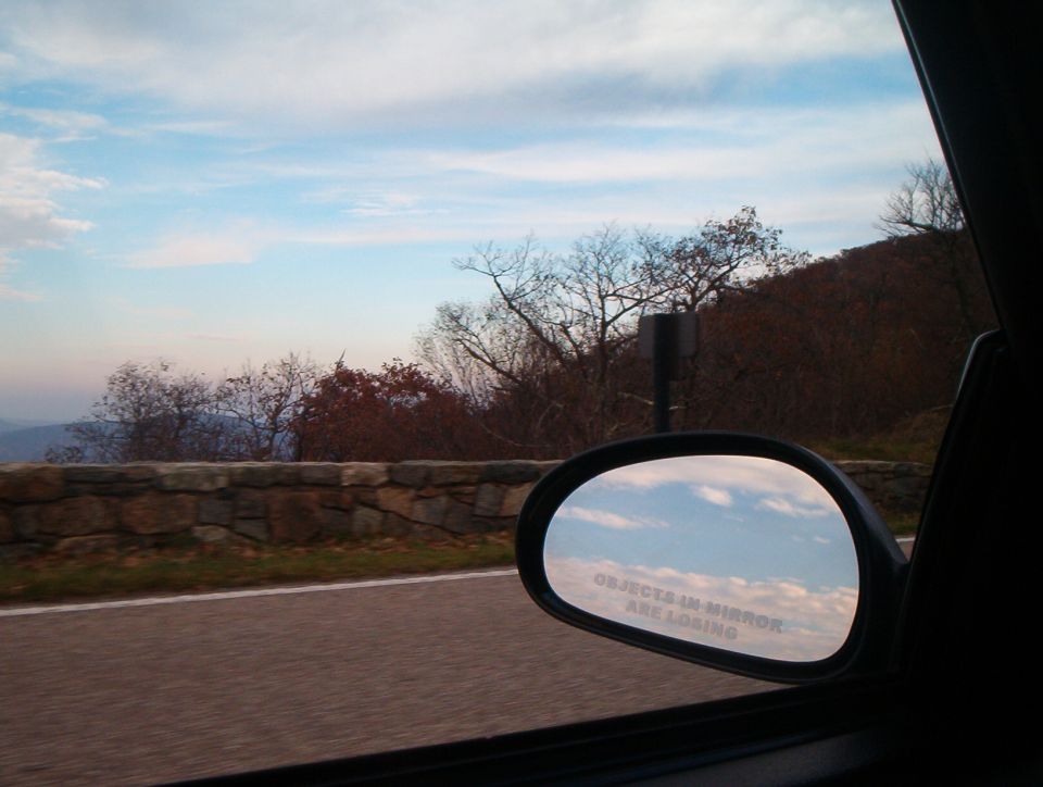 Side mirror reflecting clouds, with text 'Objects in mirror are closer than they appear'