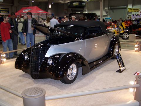 1995 Ford Probe - A custom hot rod convertible is showcased at an indoor event, with other vehicles visible in the background.