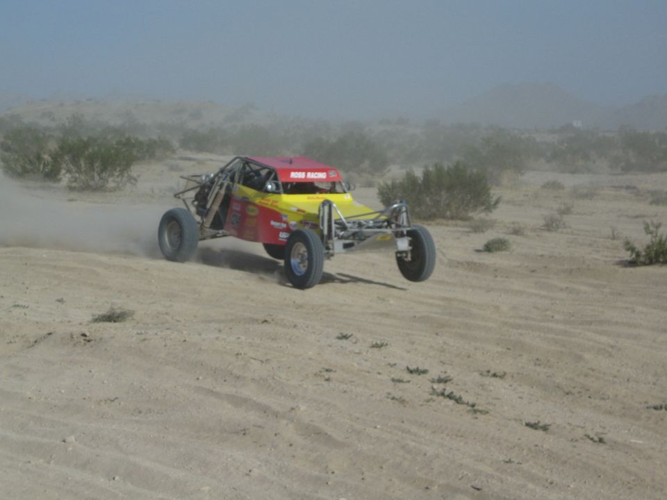 Yellow off-road buggy with Ross Racing decal jumping over a desert berm